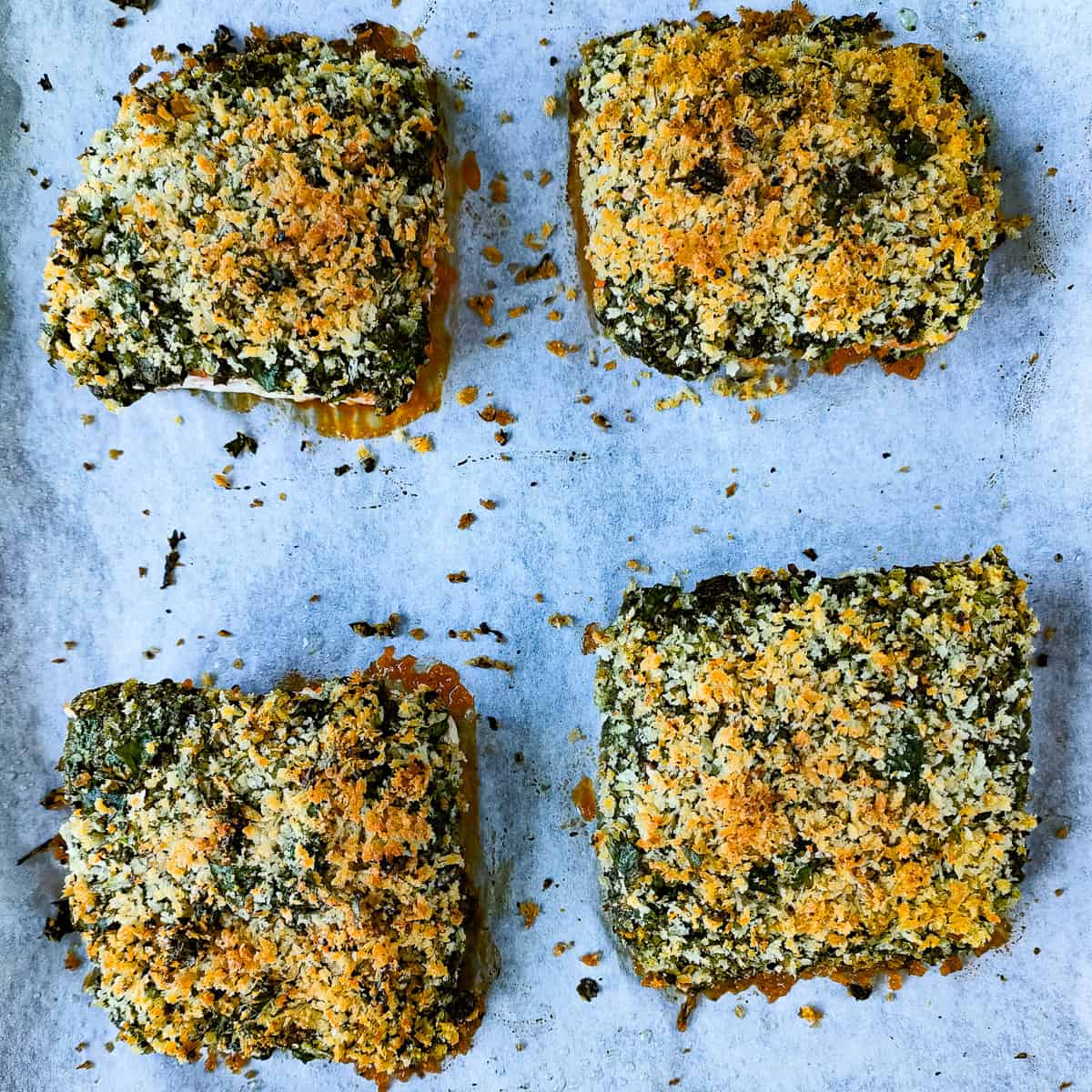 Baked pesto crusted salmon on a lined baking tray.