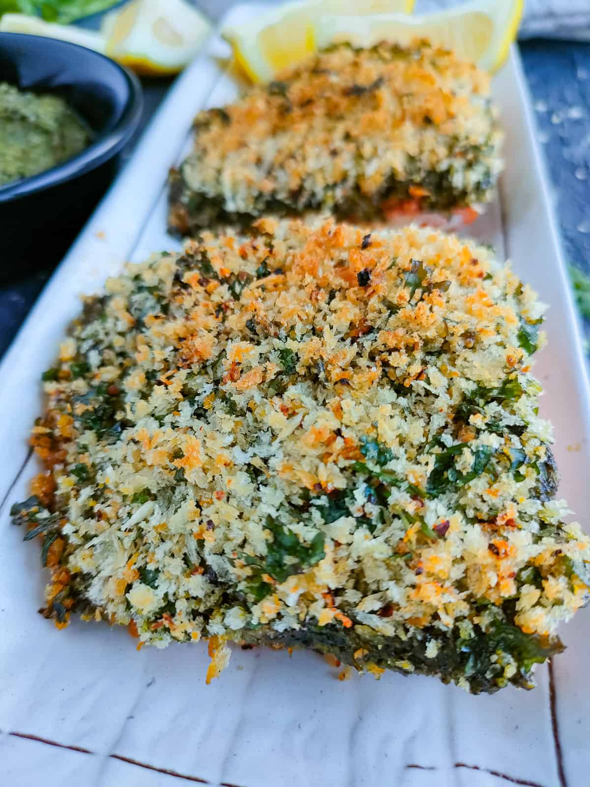 Baked pesto crusted salmon fillets on a white plate.