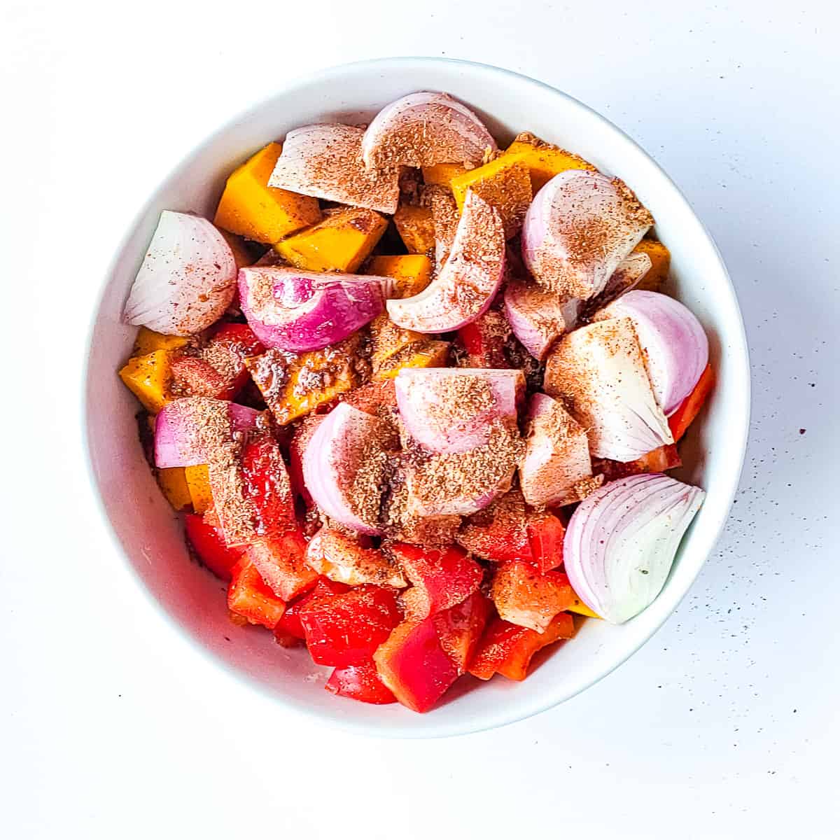 Pumpkin spice being sprinkled on diced vegetables in a white bowl.