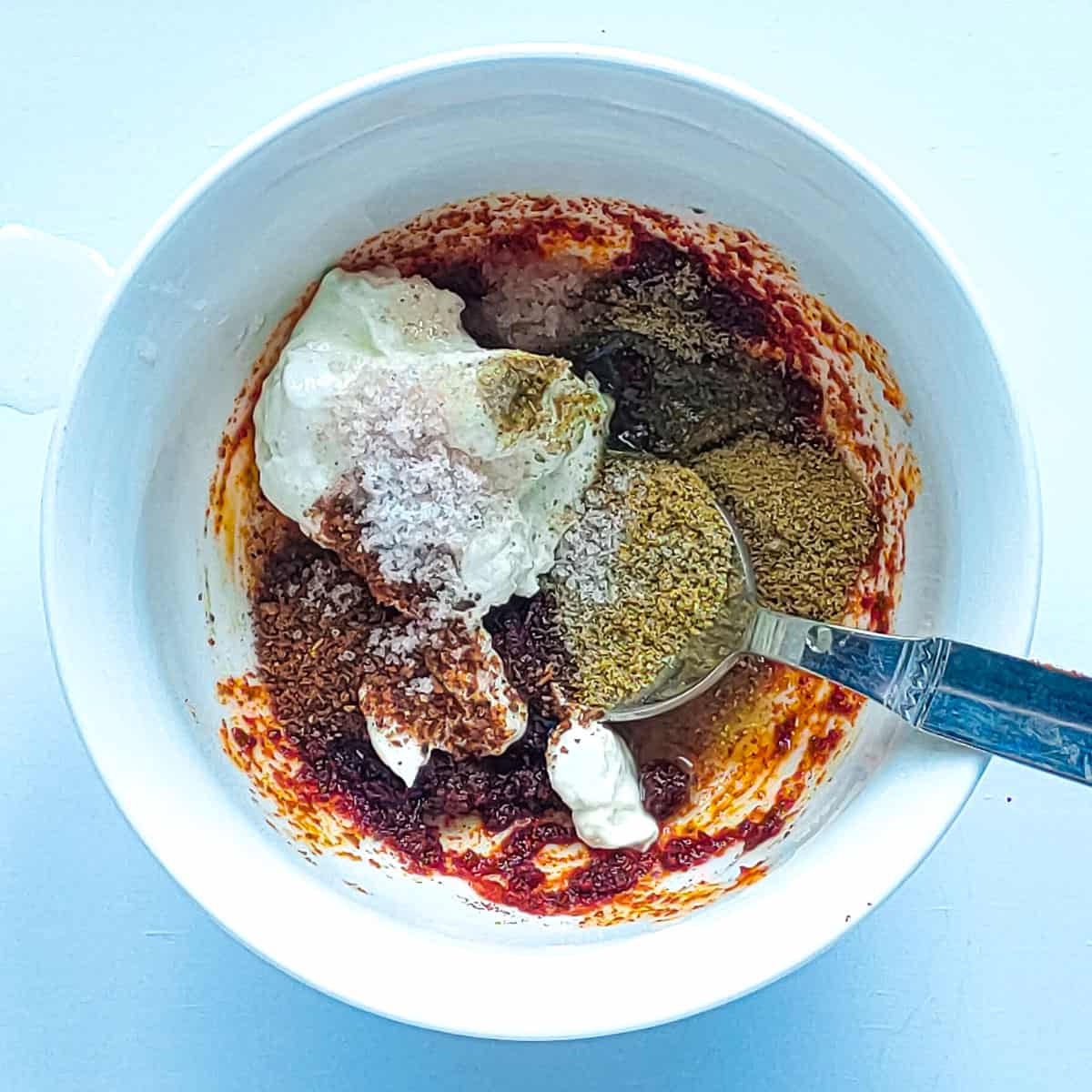 Yogurt and spices for Tandoori marinade in a white bowl with a spoon in it.