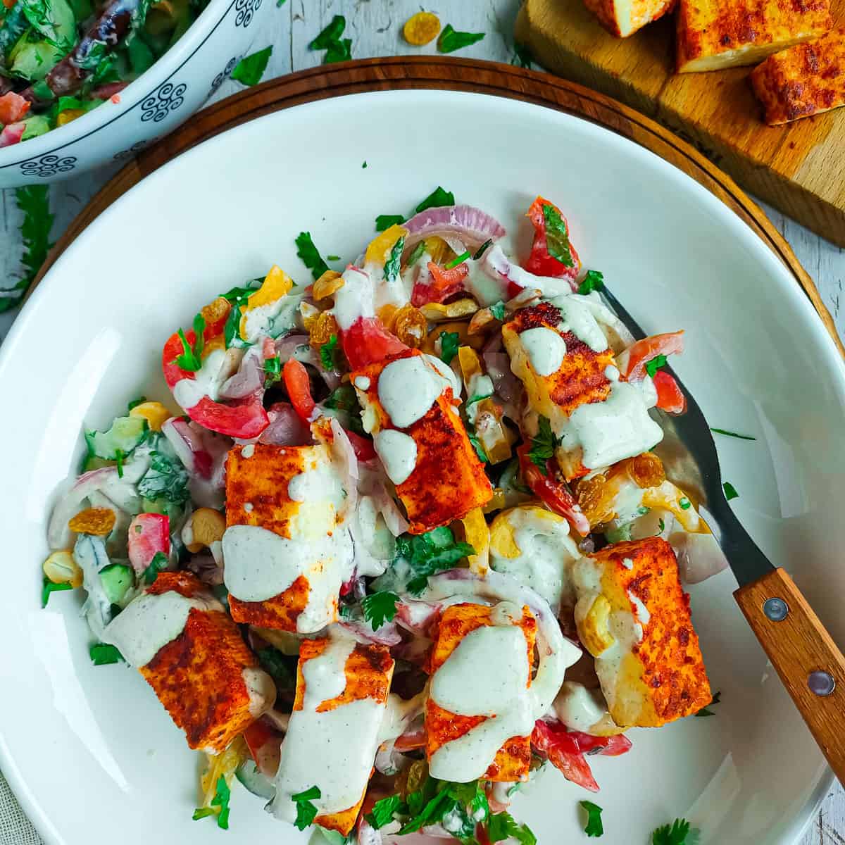 Grilled paneer salad on a white plate with a fork, paneer tikka on a board and vegetables in a bowl.