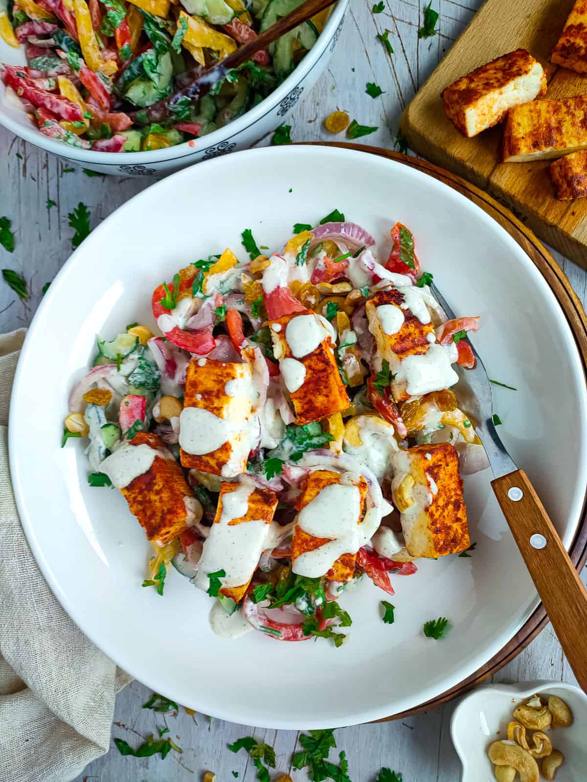 Grilled paneer salad on a white plate with a fork, paneer tikka on a board and vegetables in a bowl.