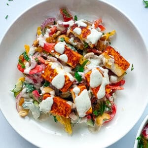 Paneer tikka salad on a white plate with a fork, paneer tikka on a board and vegetables in a bowl.