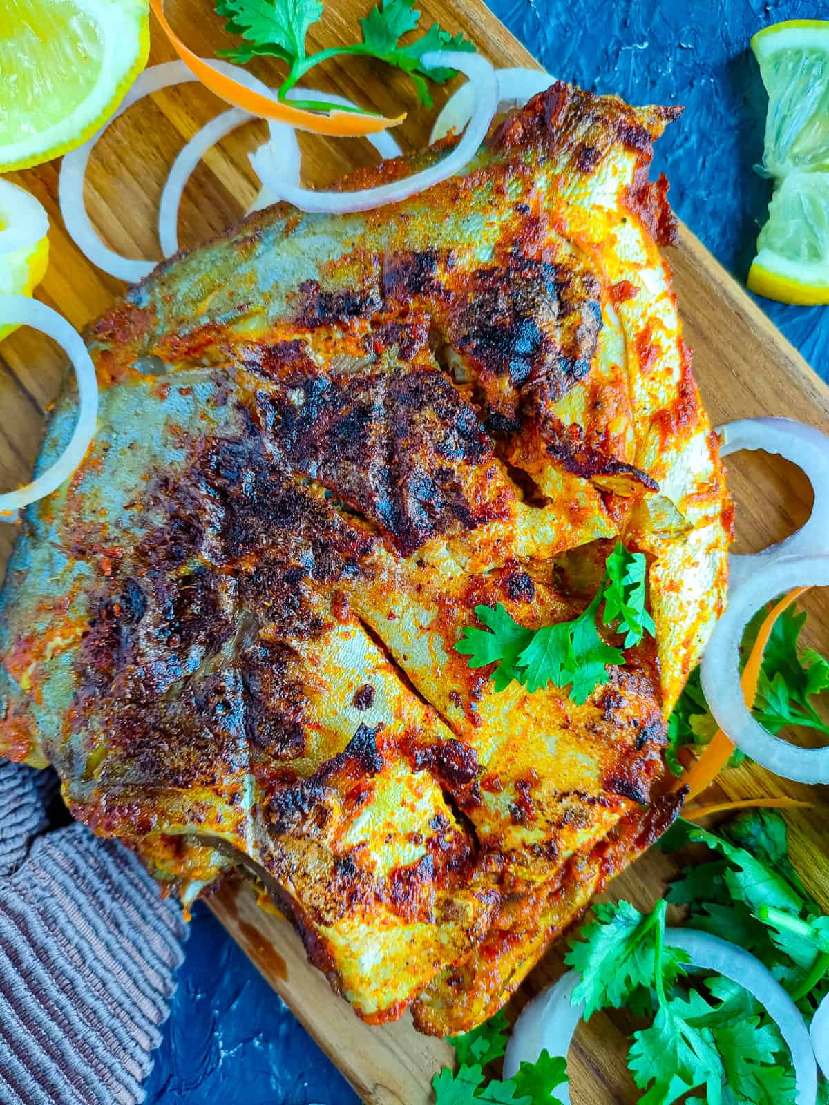 Tandoori pomfret fish on a wooden board with garnish.