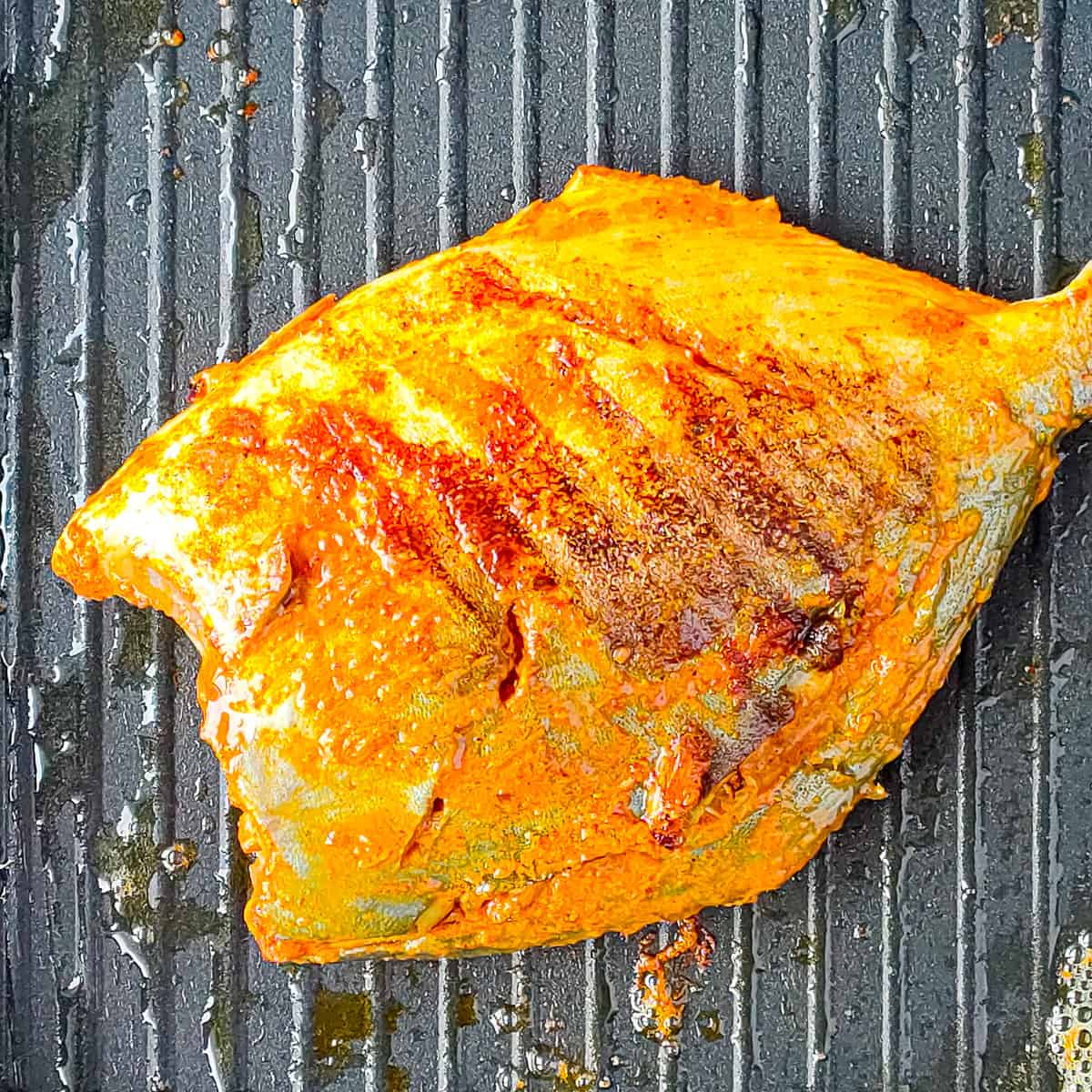 Tandoori pomfret being browned on a grill pan.
