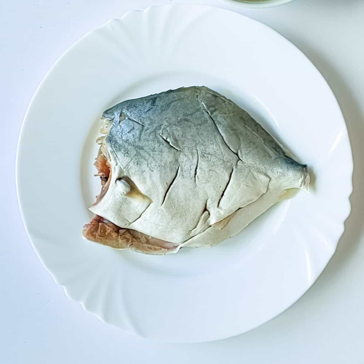 Scored pomfret on a white plate ready to be marinated.