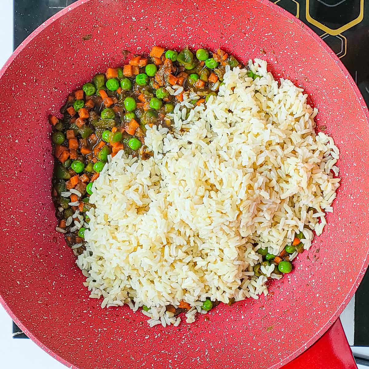 Rice being added to cooked mixed veggies in a wok pan.