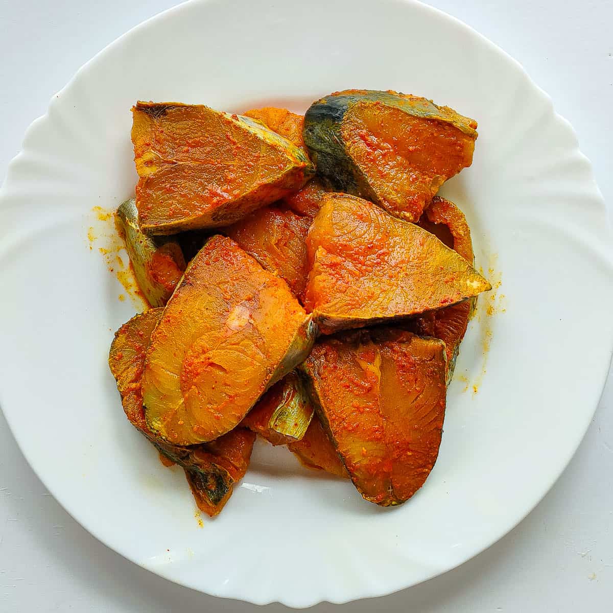 Mackerel fish seasoned with spices on a white plate.