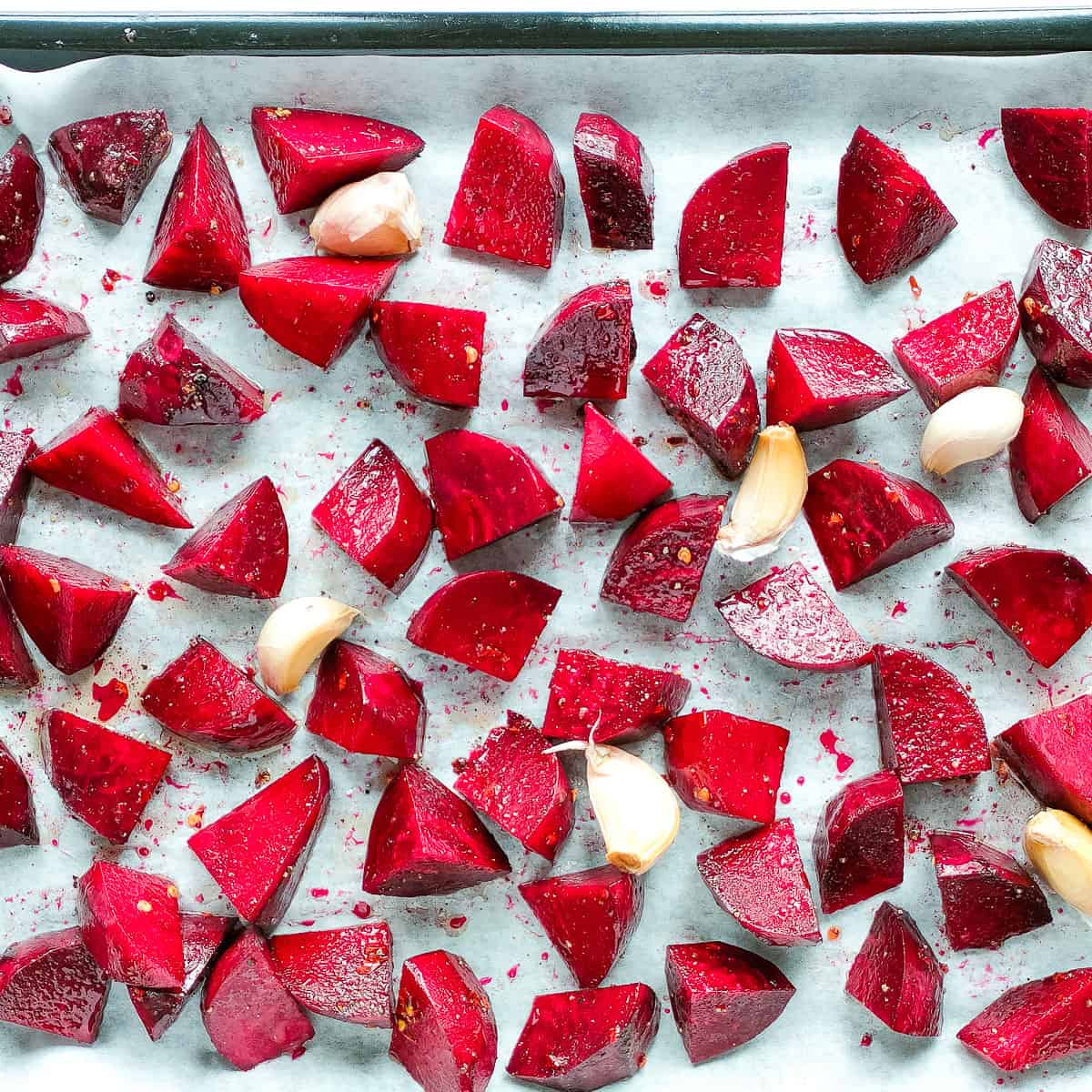 Seasoned beetroot cubes and garlic ready for roasting on a baking sheet.