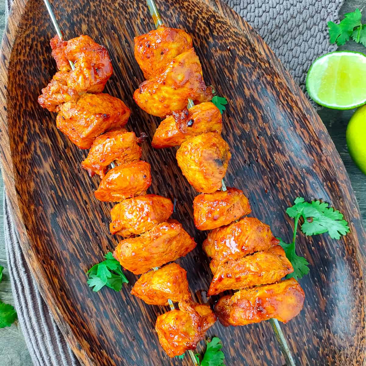 Tandoori chicken tikka skewers on a wooden plate.