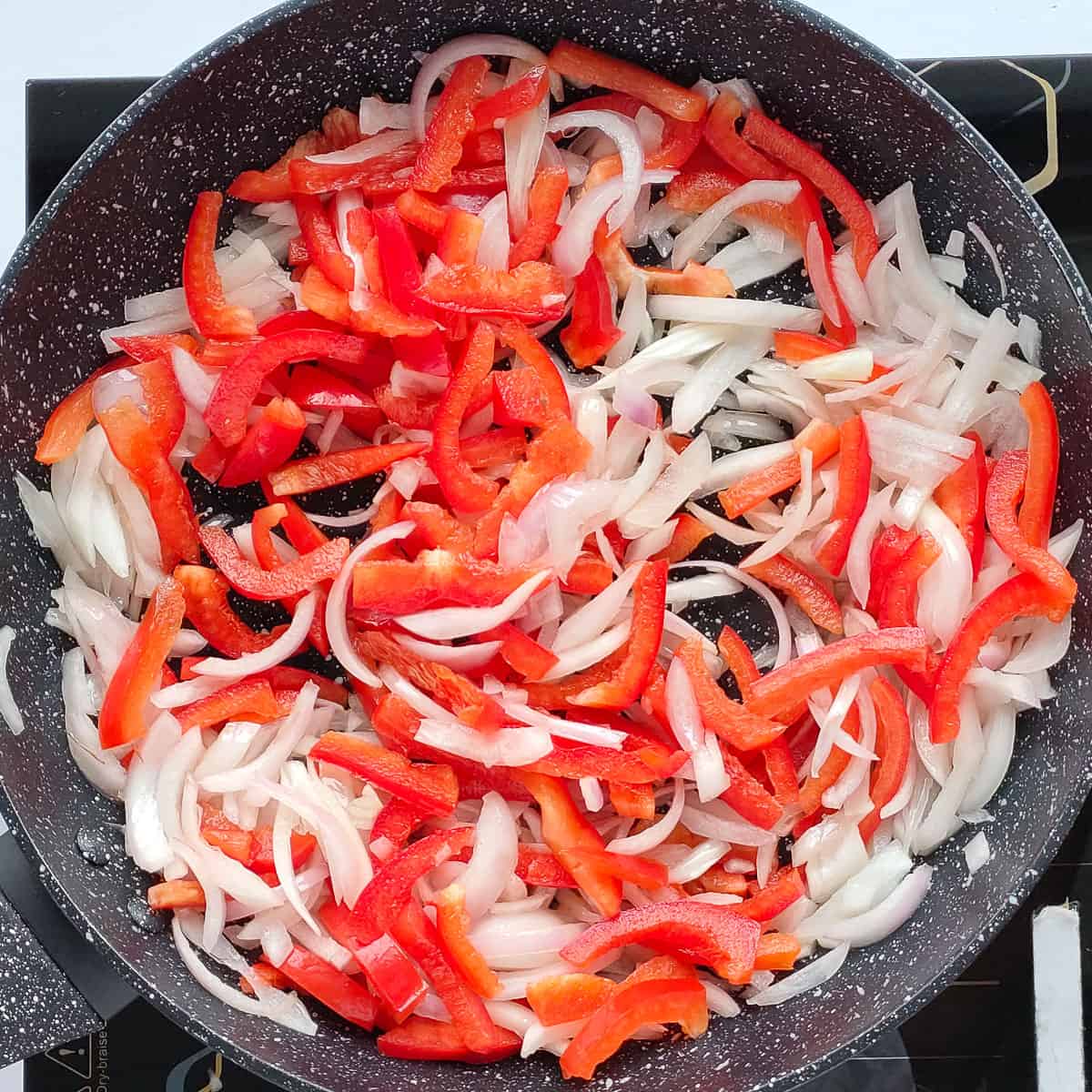 Onions and bell peppers being sauteed in a pan.