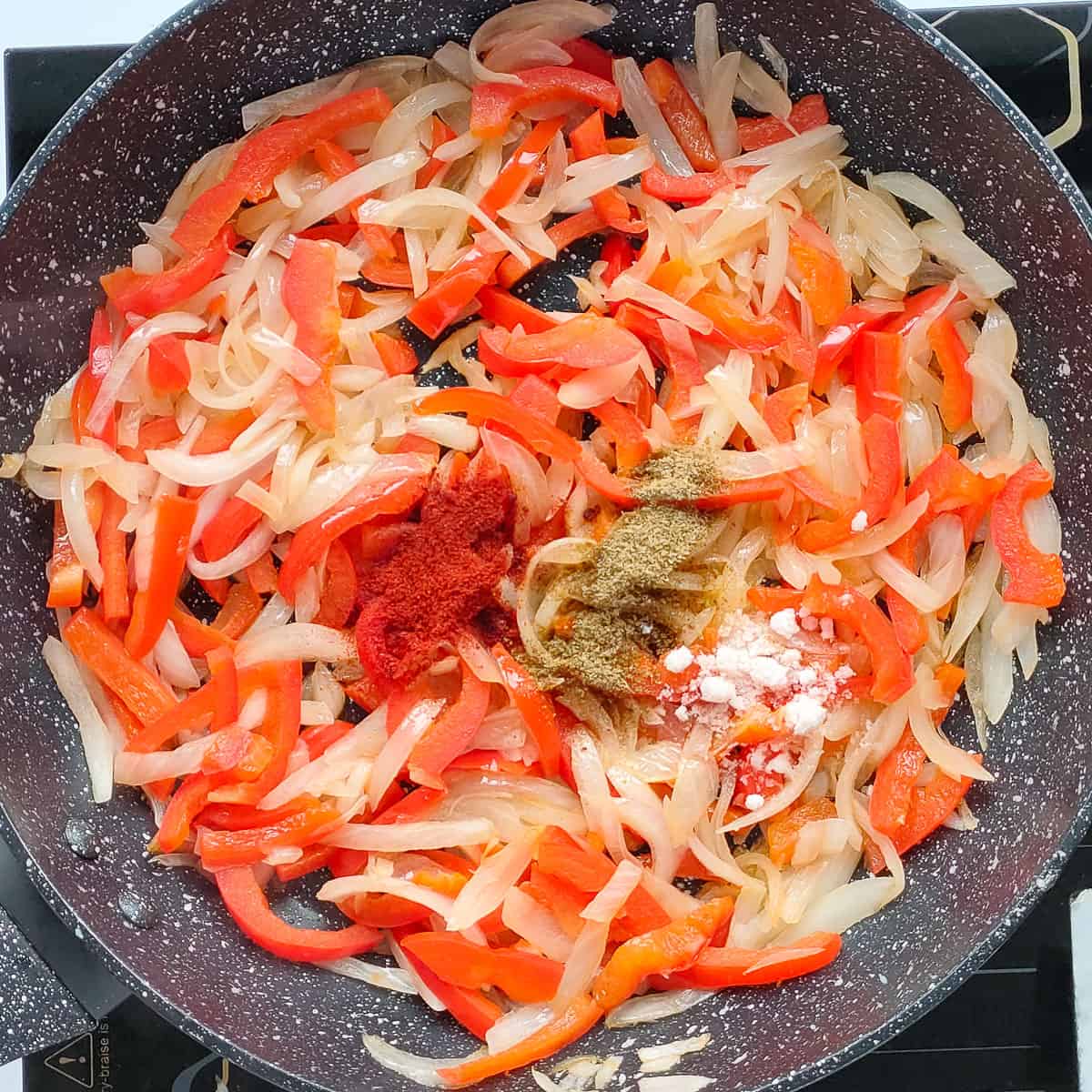 Spices added to sauteed onions and bell peppers in a pan.