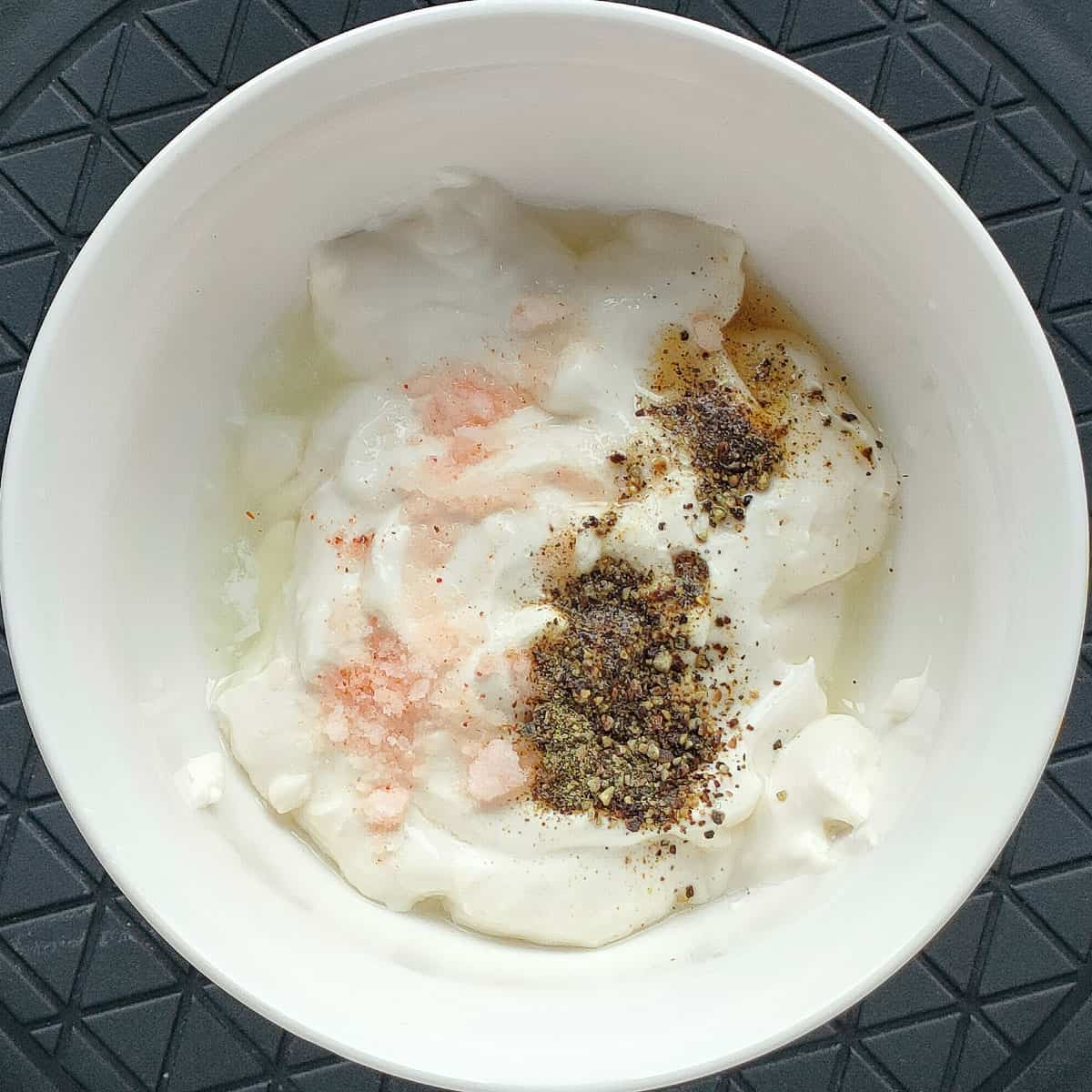 Black pepper and salt added to yogurt for sauce in a small bowl.