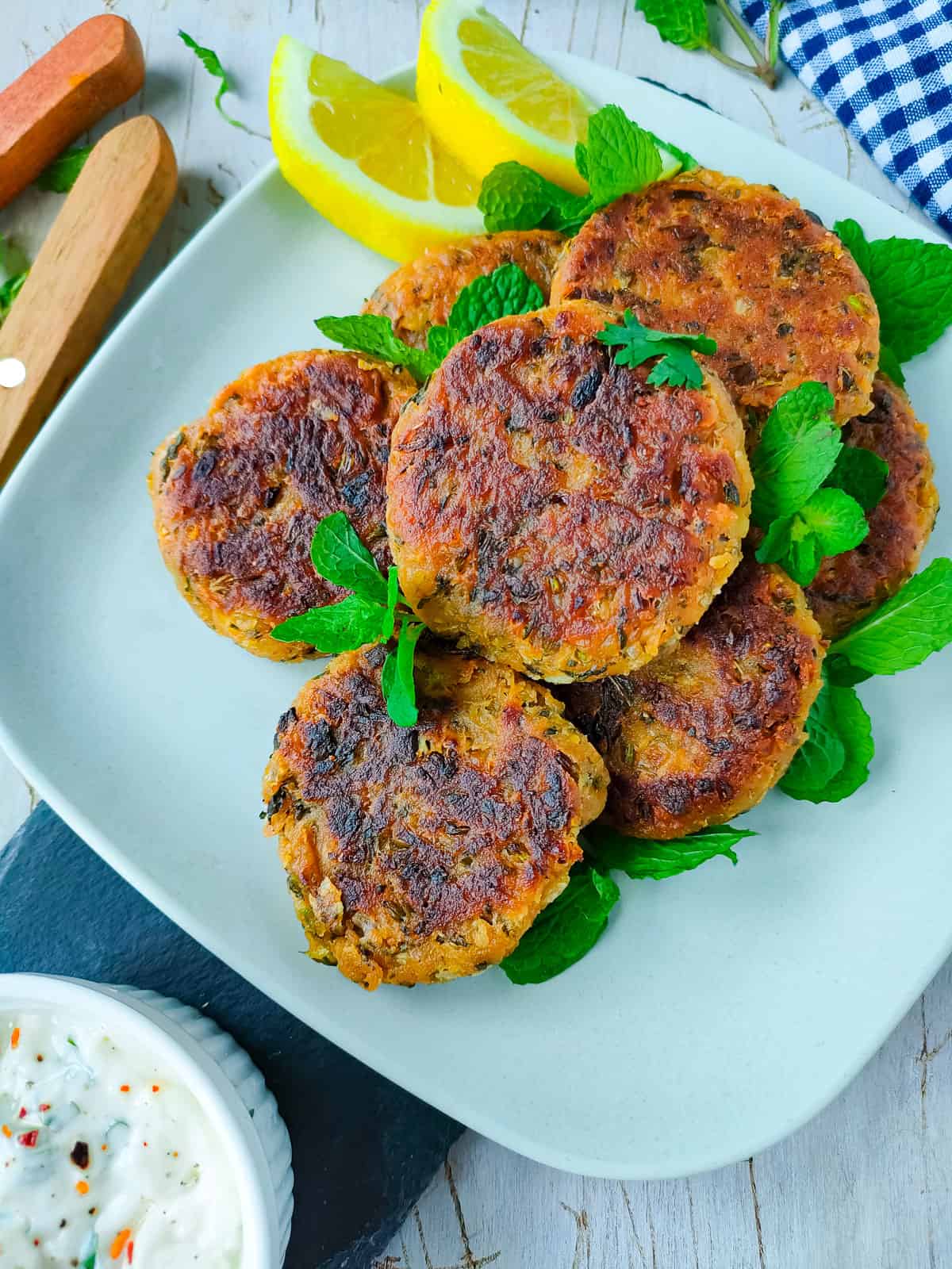 Chana kababs on an off-white plate with yogurt sauce in a small white bowl.