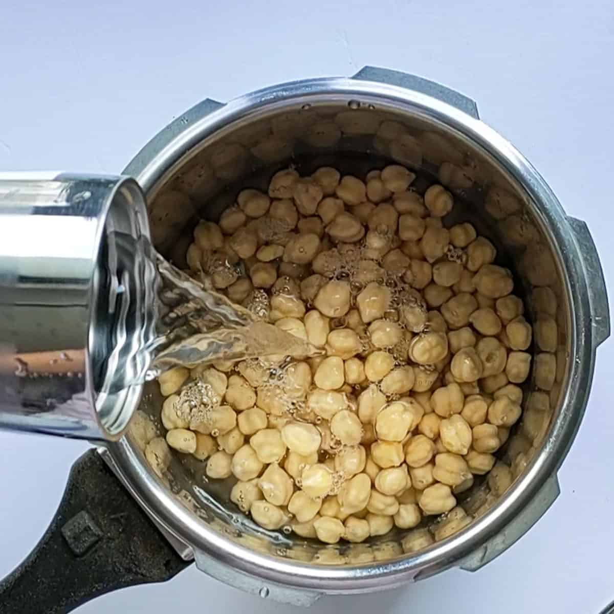 Water being added to soaked chickpeas in a pressure cooker.