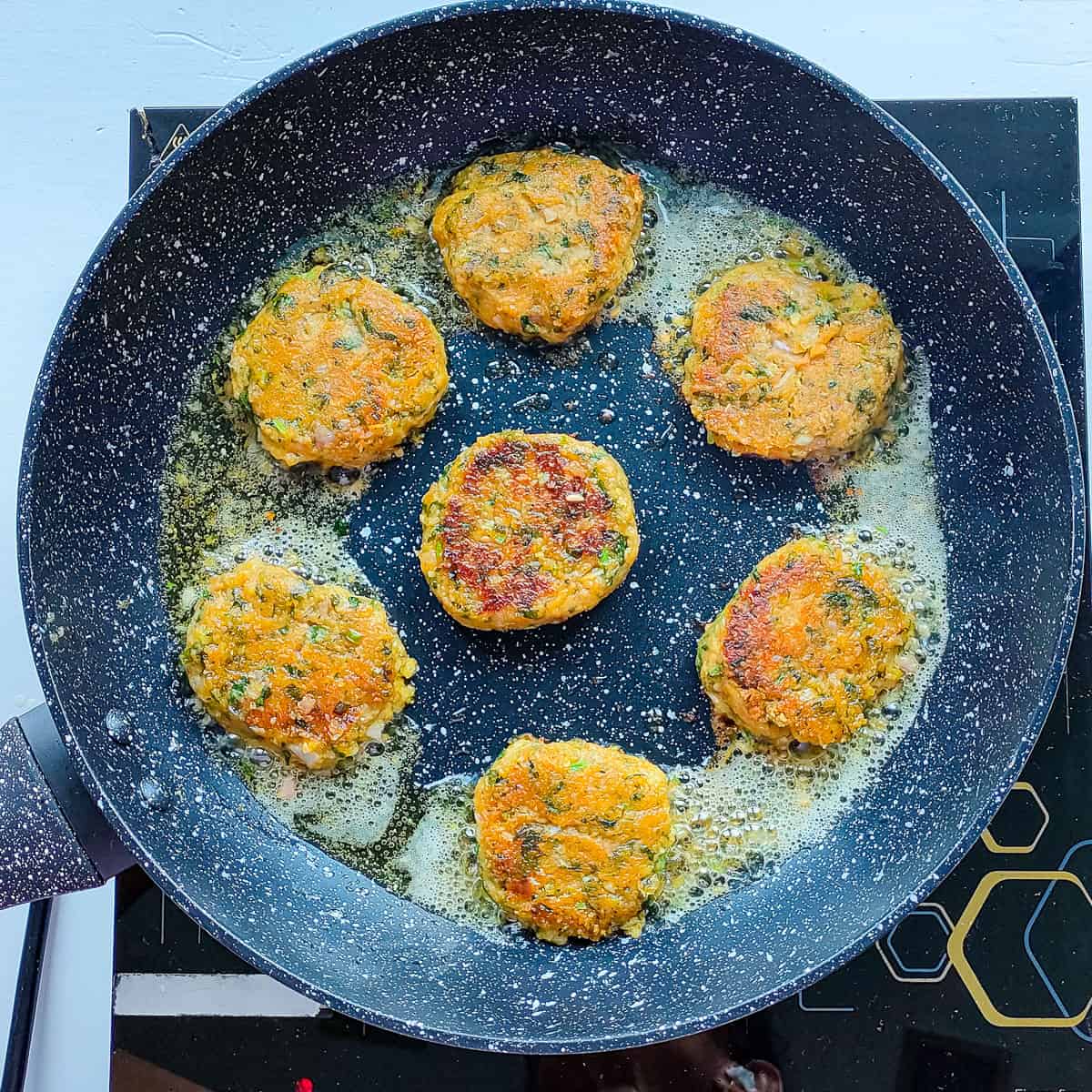 Chickpea patties being pan-fried in a black pan.