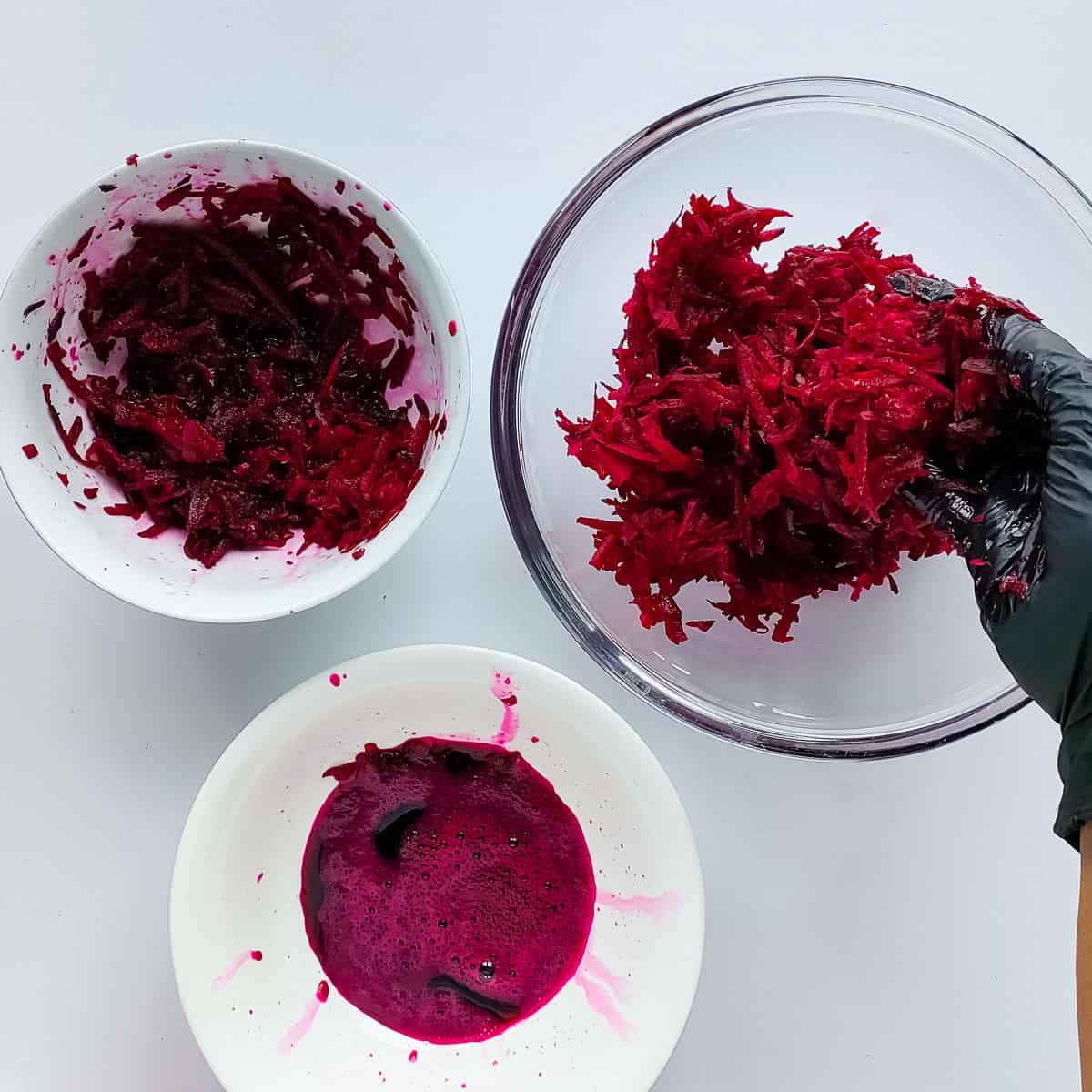 Water being squeezed out of grated beetroot in separate bowls.