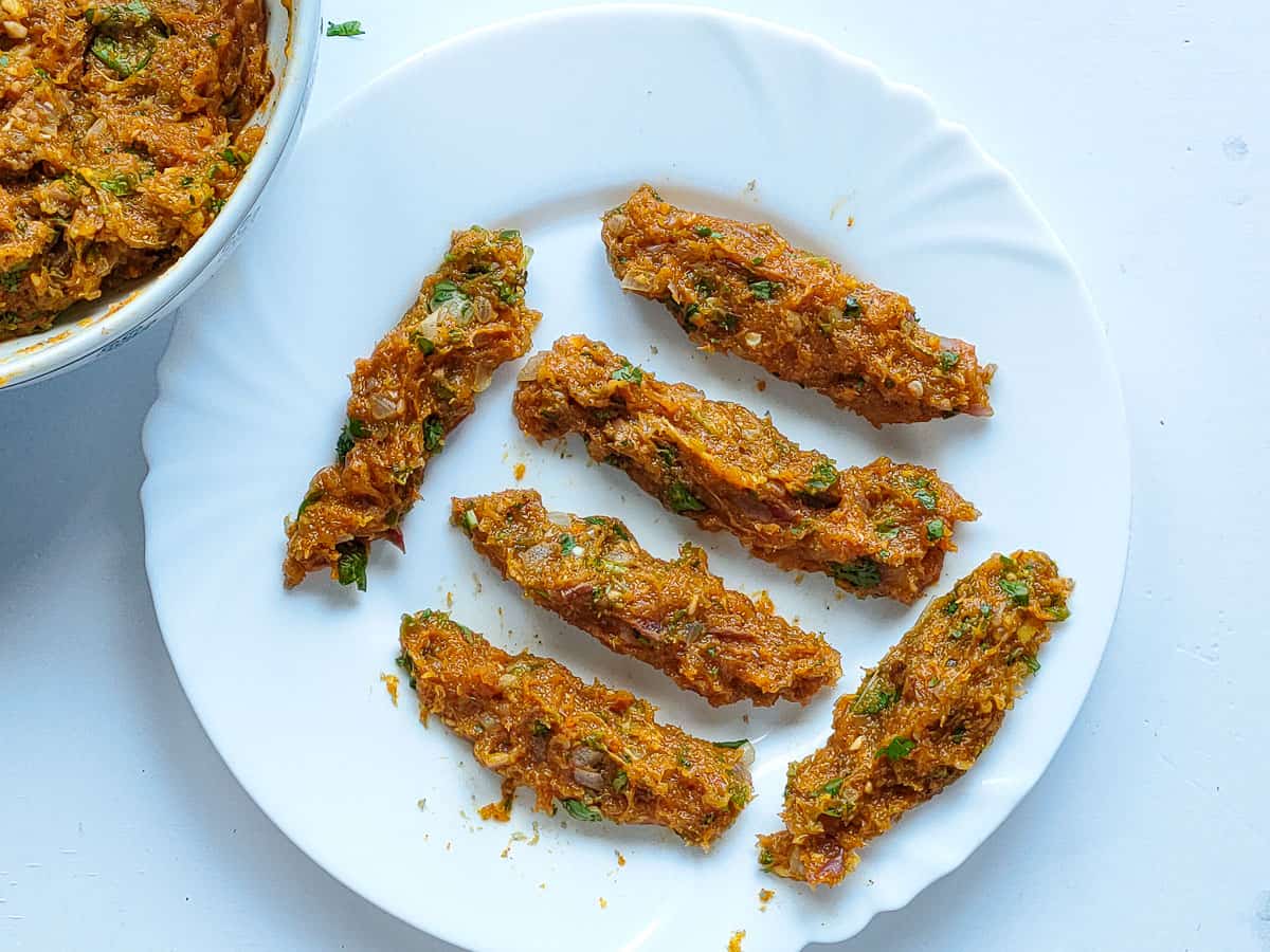 Minced chicken with spices shaped into kebabs on a white plate.