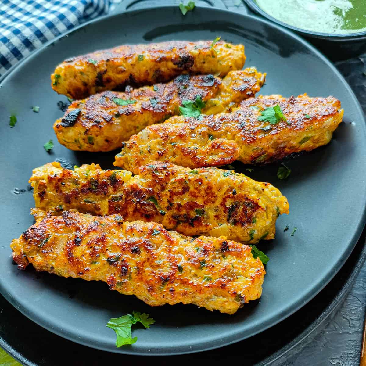 Chicken mince kebabs on a black plate.