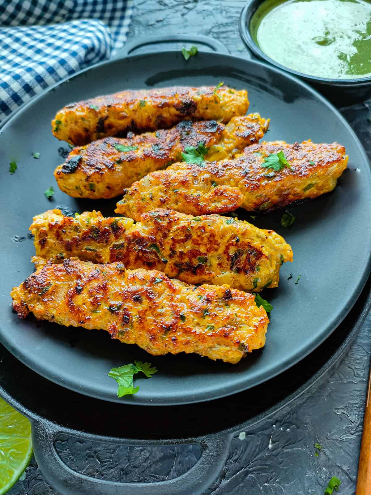 Minced chicken kebabs on a black plate.
