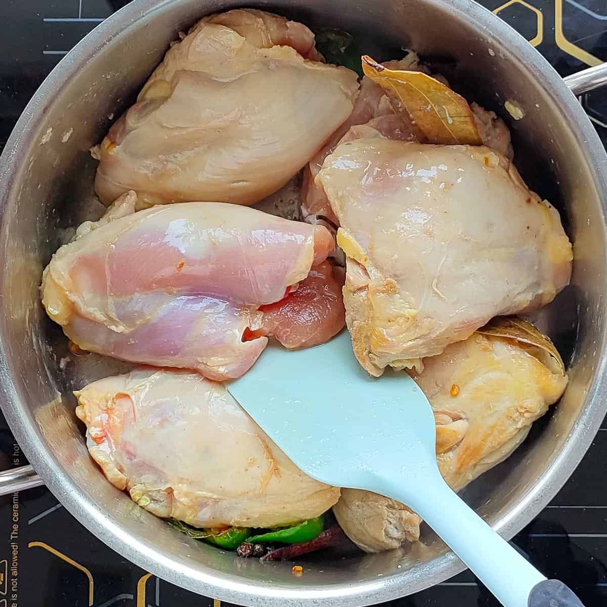 Chicken being sauteed in a metal soup pot for broth.