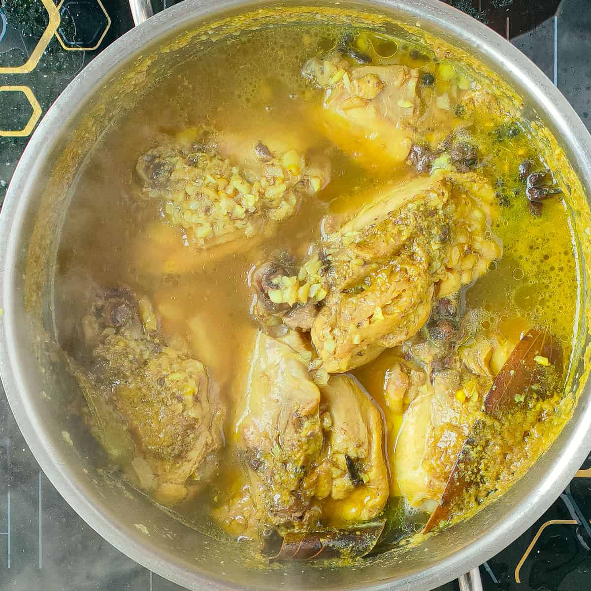 Chicken thighs simmering in the broth in a metal soup pot.