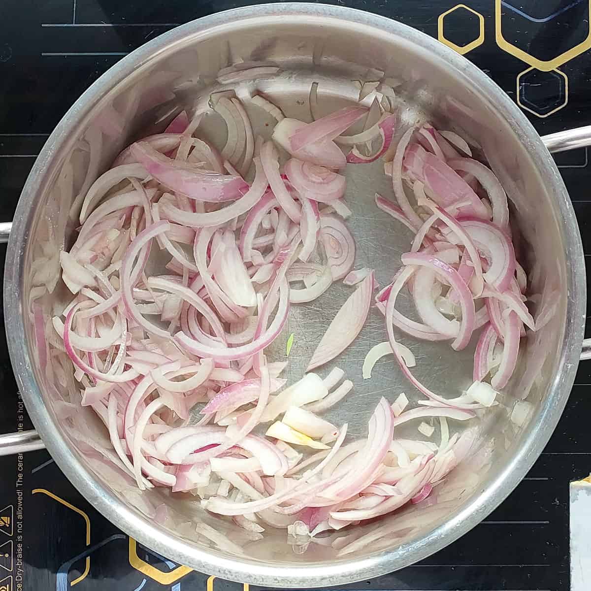 Sliced onion being sauteed in a metal soup pot.