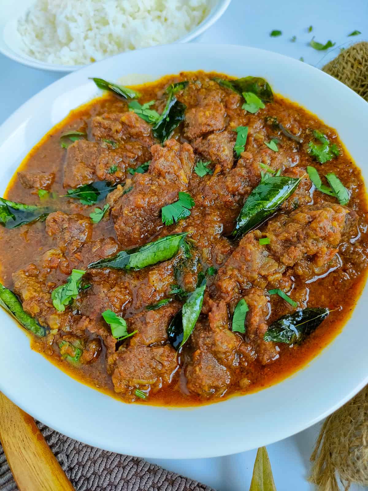 Pressure cooker mutton curry in a white bowl with a bowl of rice next to it.