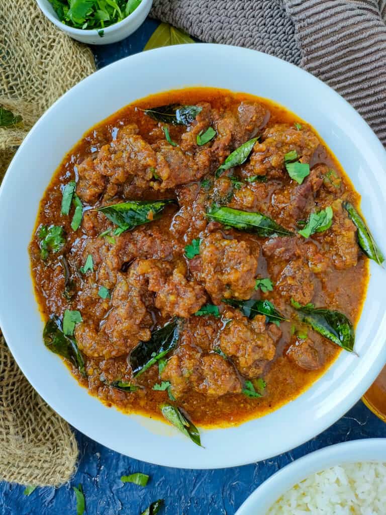 Goat masala in a white bowl with a bowl of rice next to it.