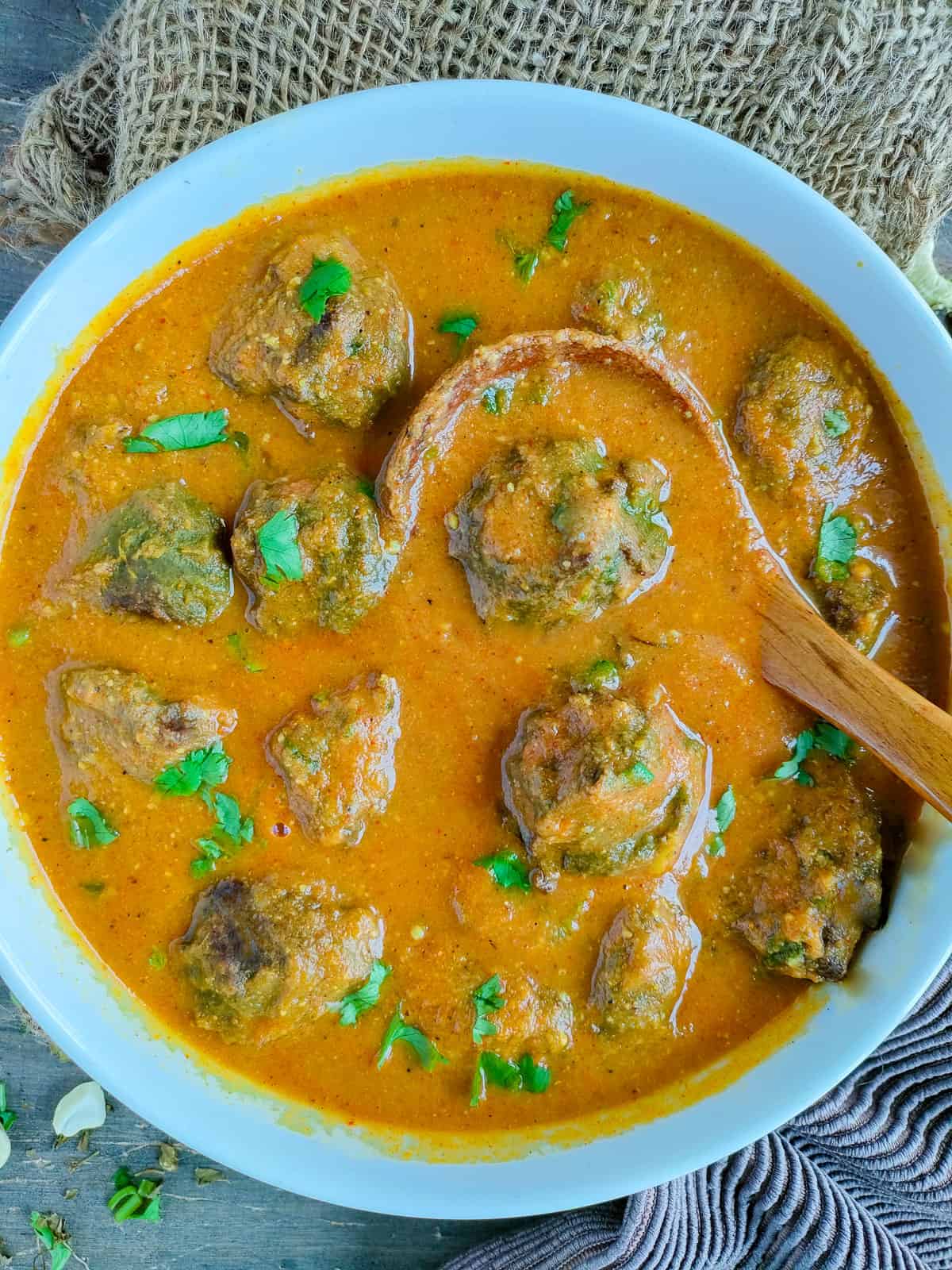 Spinach kofta curry in a white bowl with a ladle in it.