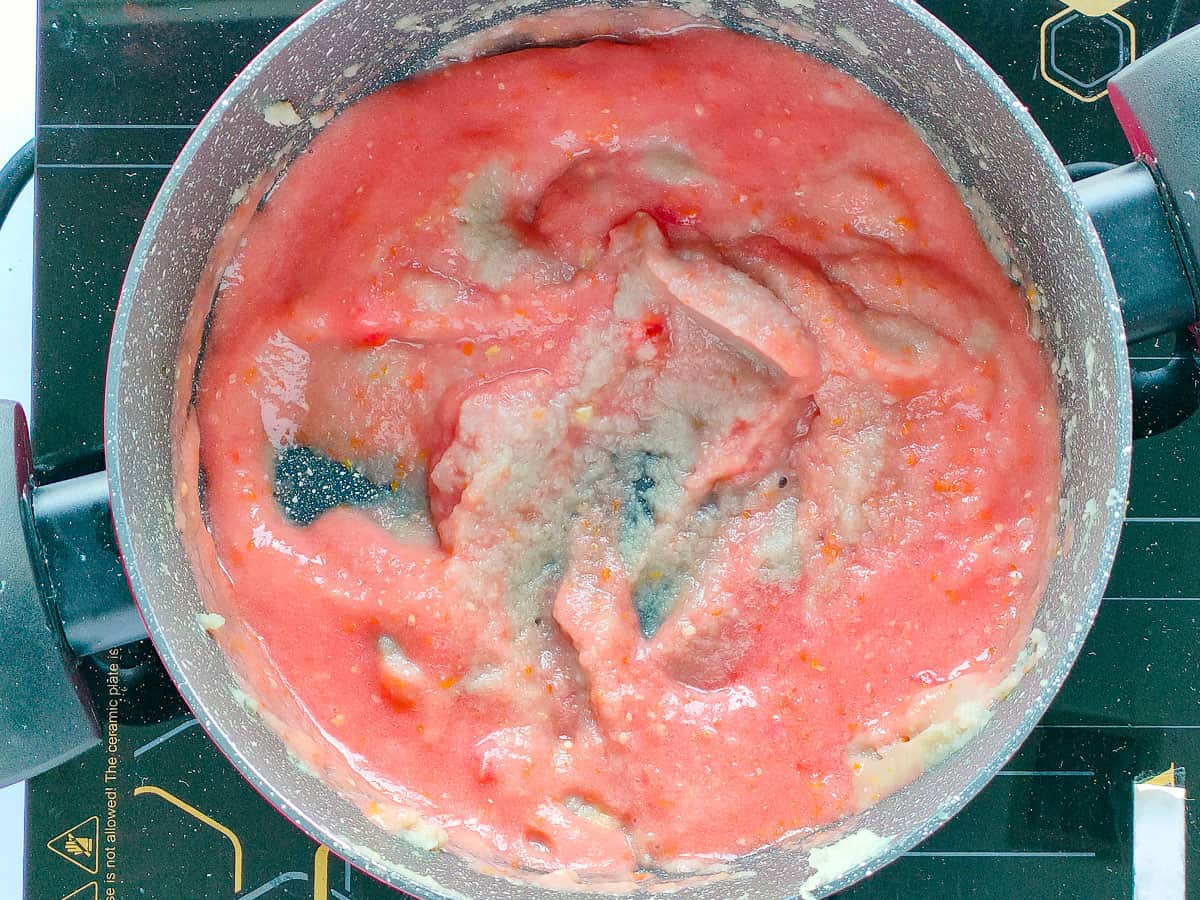 Tomato puree being cooked with blended onions in a cooking pot.