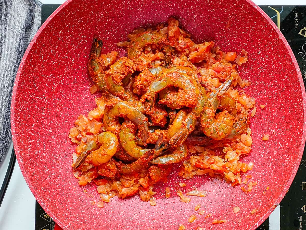Marinated prawns with sauteed onions and tomatoes in a non-stick pan.
