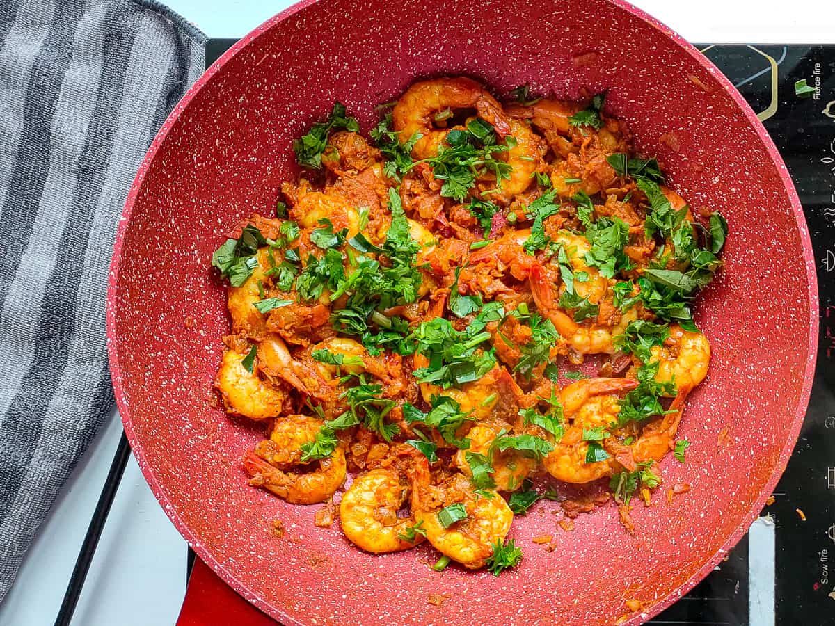 Jhinga masala garnished with coriander and curry leaves in a non-stick pan.