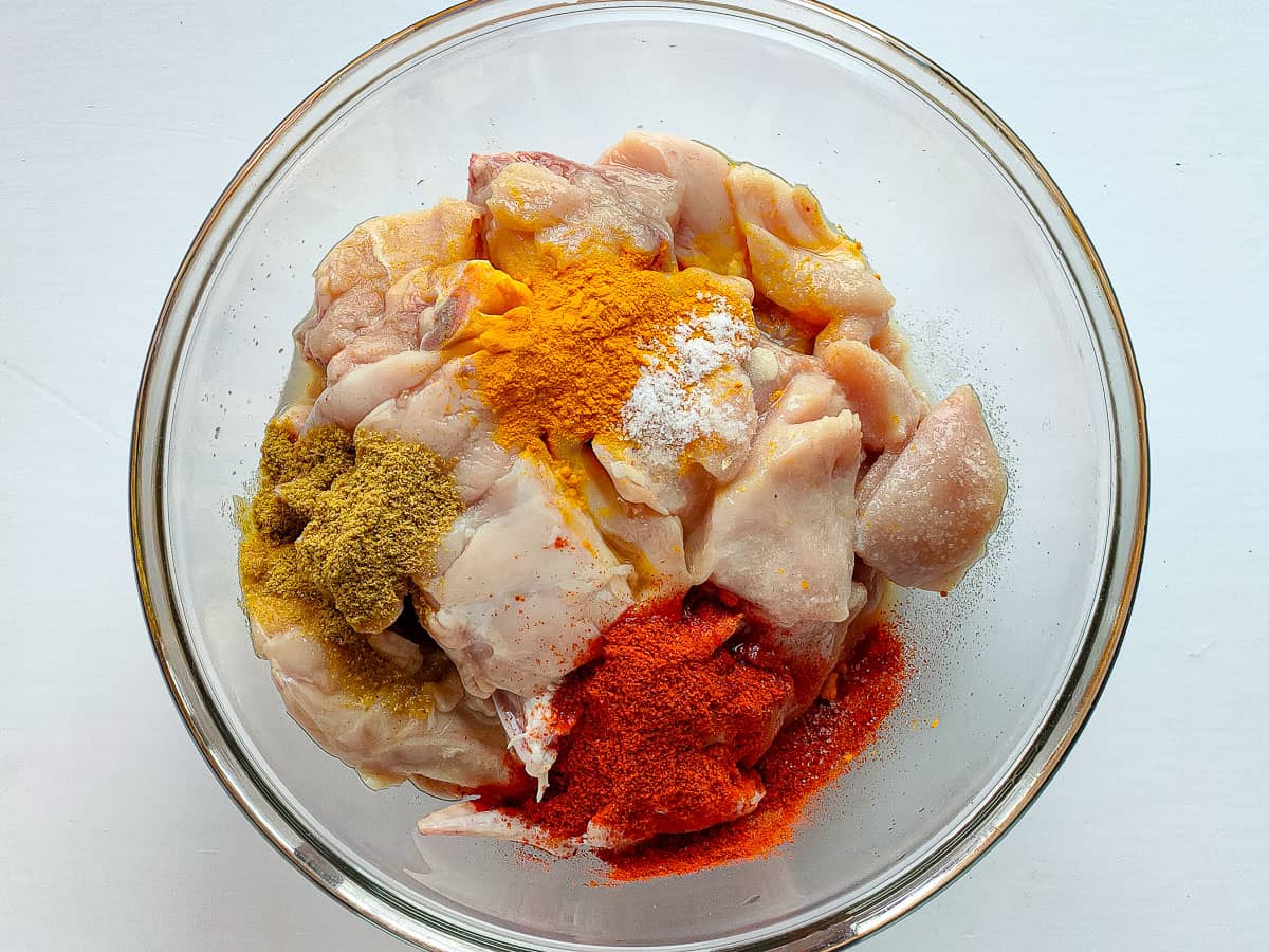 Chicken with spices for marinating in a glass bowl.