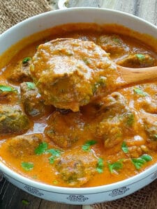 Palak kofta curry scooped out with a ladle from a white bowl full of curry.