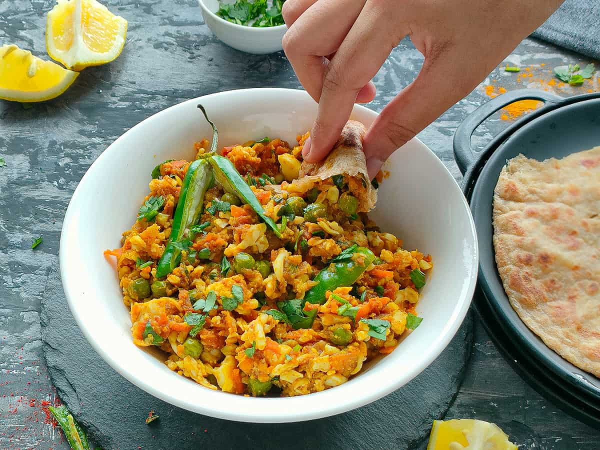 Anda keema masala in a white bowl being scooped out with a piece of roti.