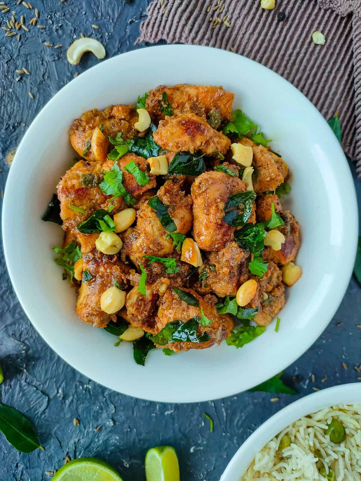 Jeera chicken with yogurt in a white bowl and a bowl of rice next to it.