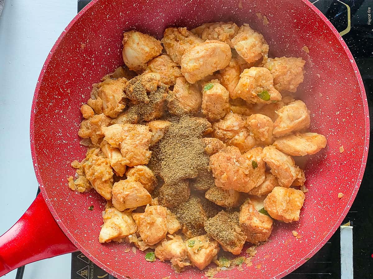 Ground spices added to sauteed chicken in a pan.