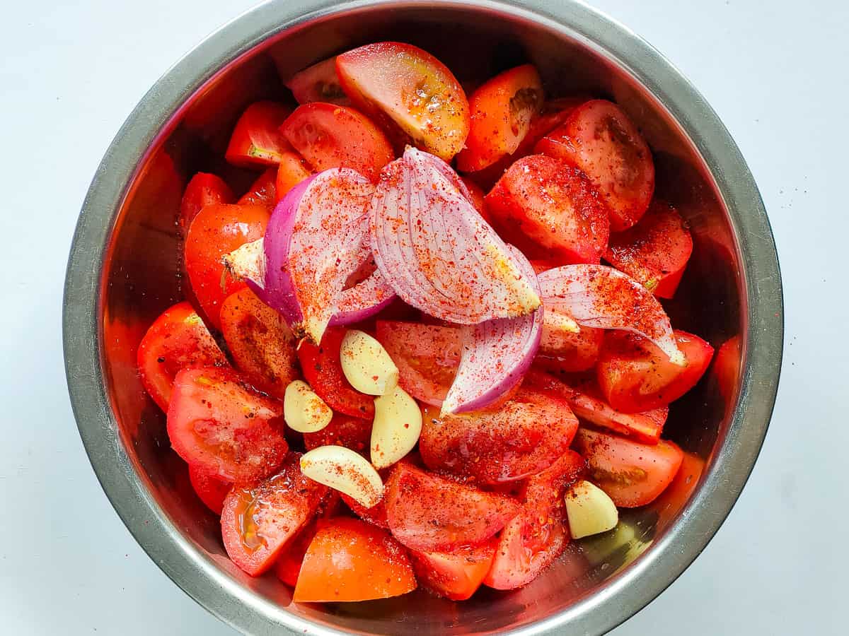 Quartered tomatoes, onions and garlic mixed with salt, chili flakes and oil in a bowl.
