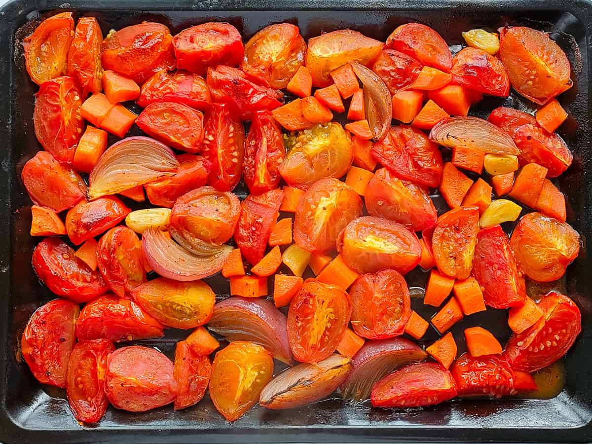 Roasted tomatoes, onions and garlic on a baking tray.