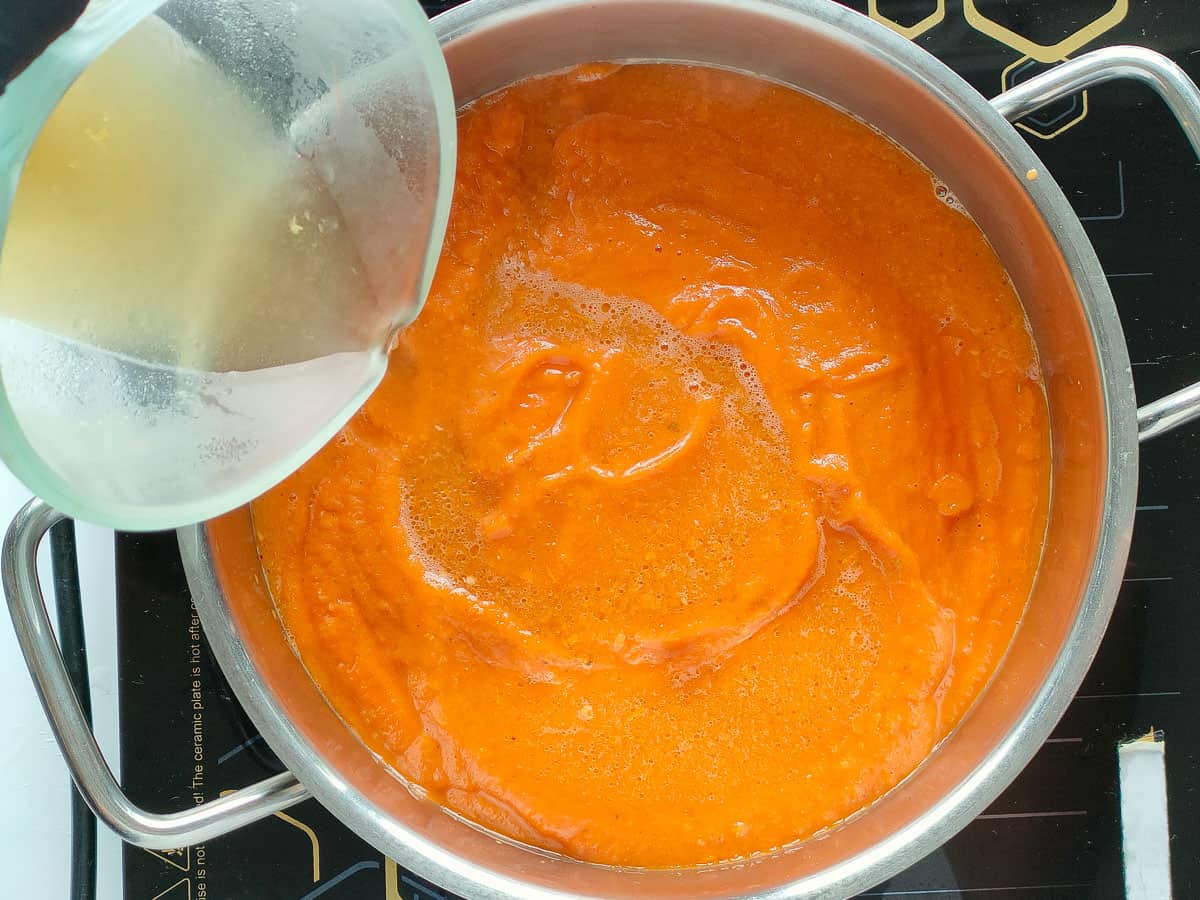 Stock added to the onion tomato mixture in a soup pot.