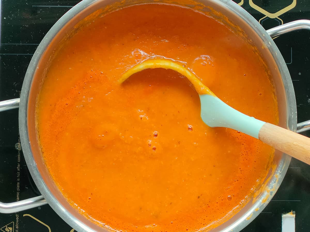 Roasted garlic and tomato soup in a soup pot with a ladle in it.