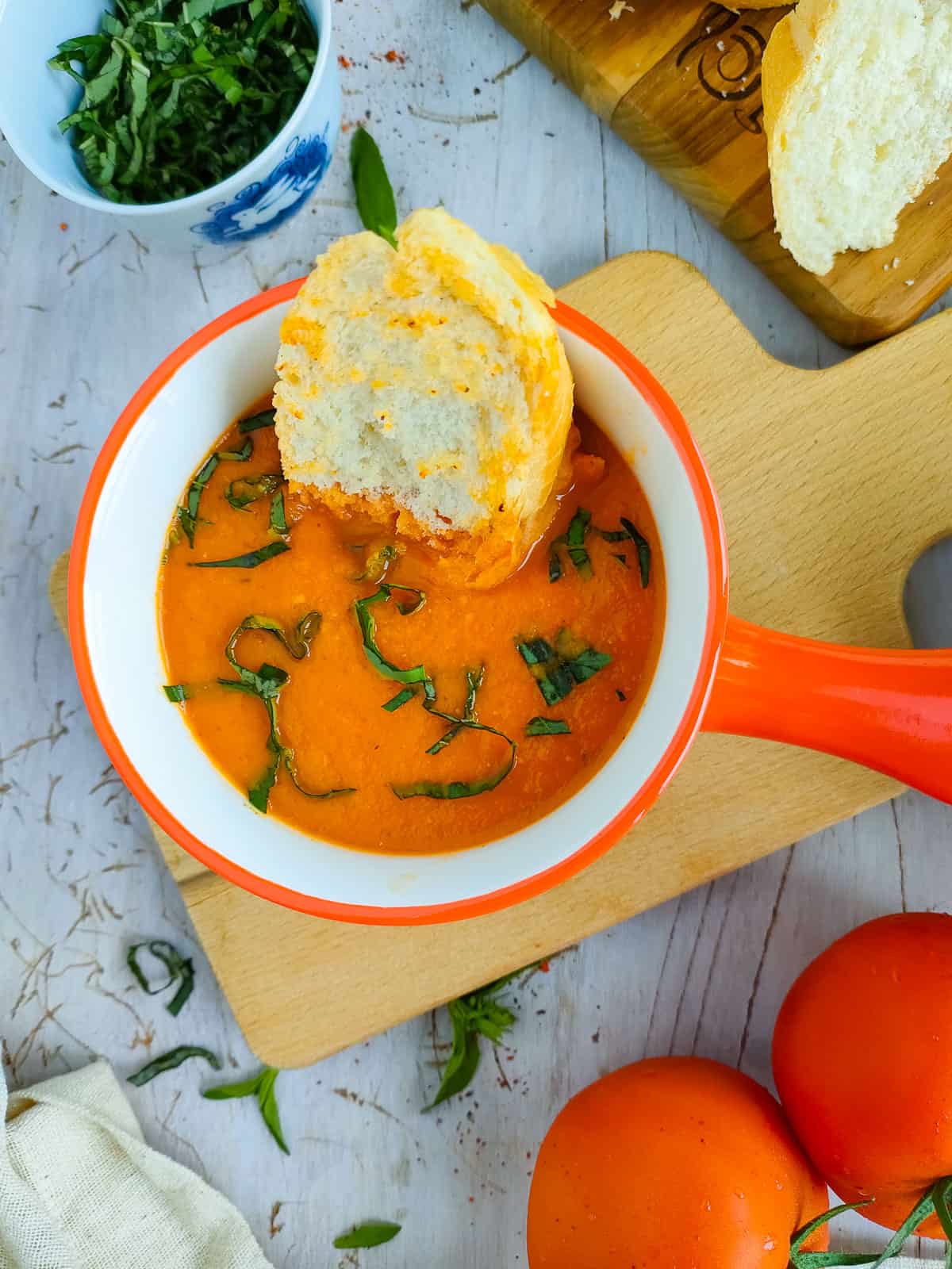 Tomato garlic soup in a red and white bowl with a piece of toast in it.