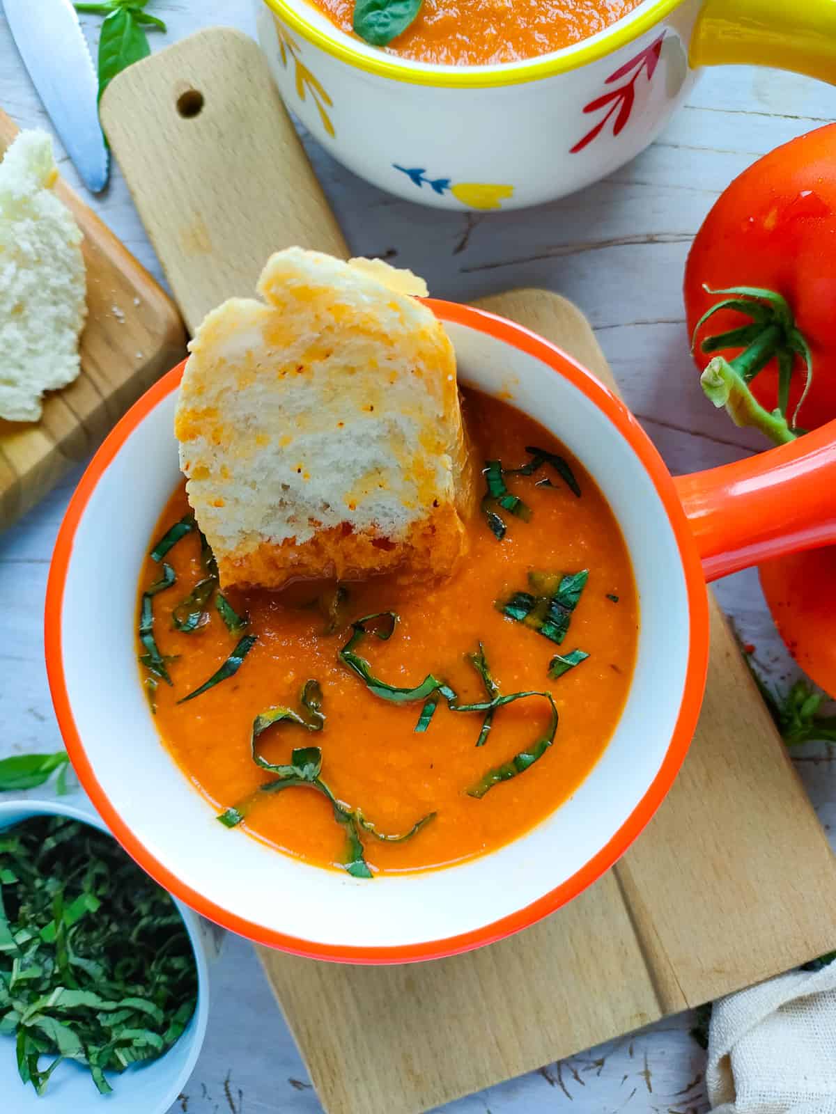 Roasted tomato garlic soup in a red and white bowl with a piece of toast in it.