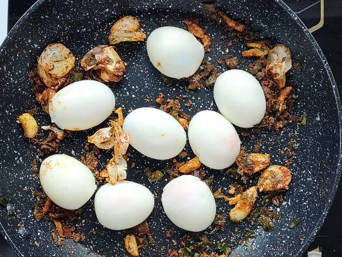 Boiled and halved eggs with spices, garlic and curry leaves in a non-stick pan.