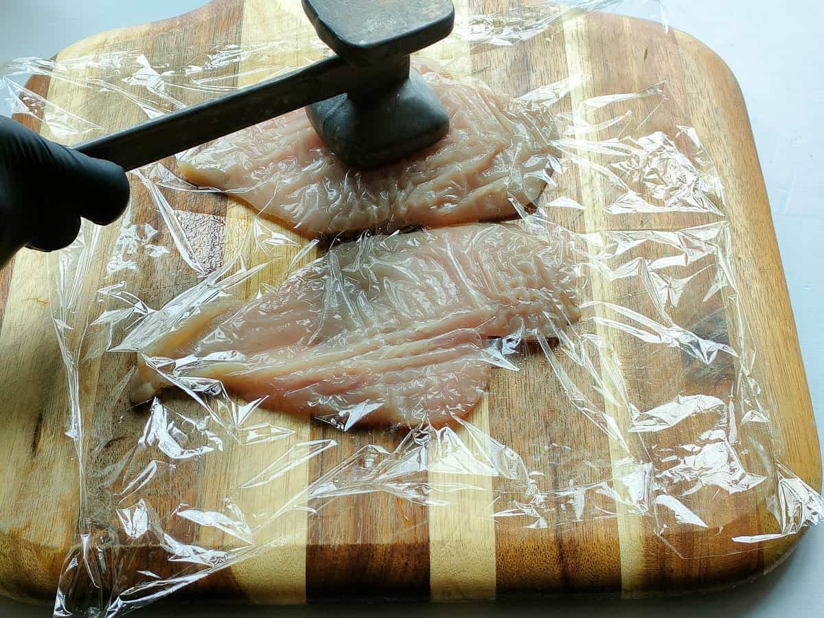 Thin sliced chicken breasts tenderized with a meat mallet on a wooden chopping board.