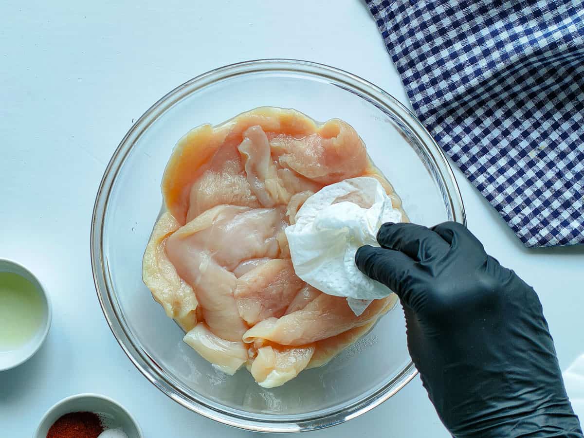 Tenderized chicken breasts in a glass bowl being blotted with a tissue.