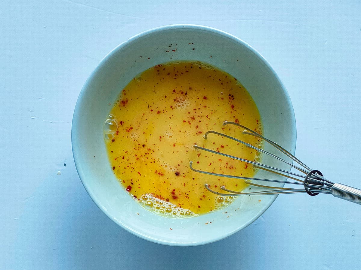 Egg beaten with salt, pepper and chili flakes in a small bowl.