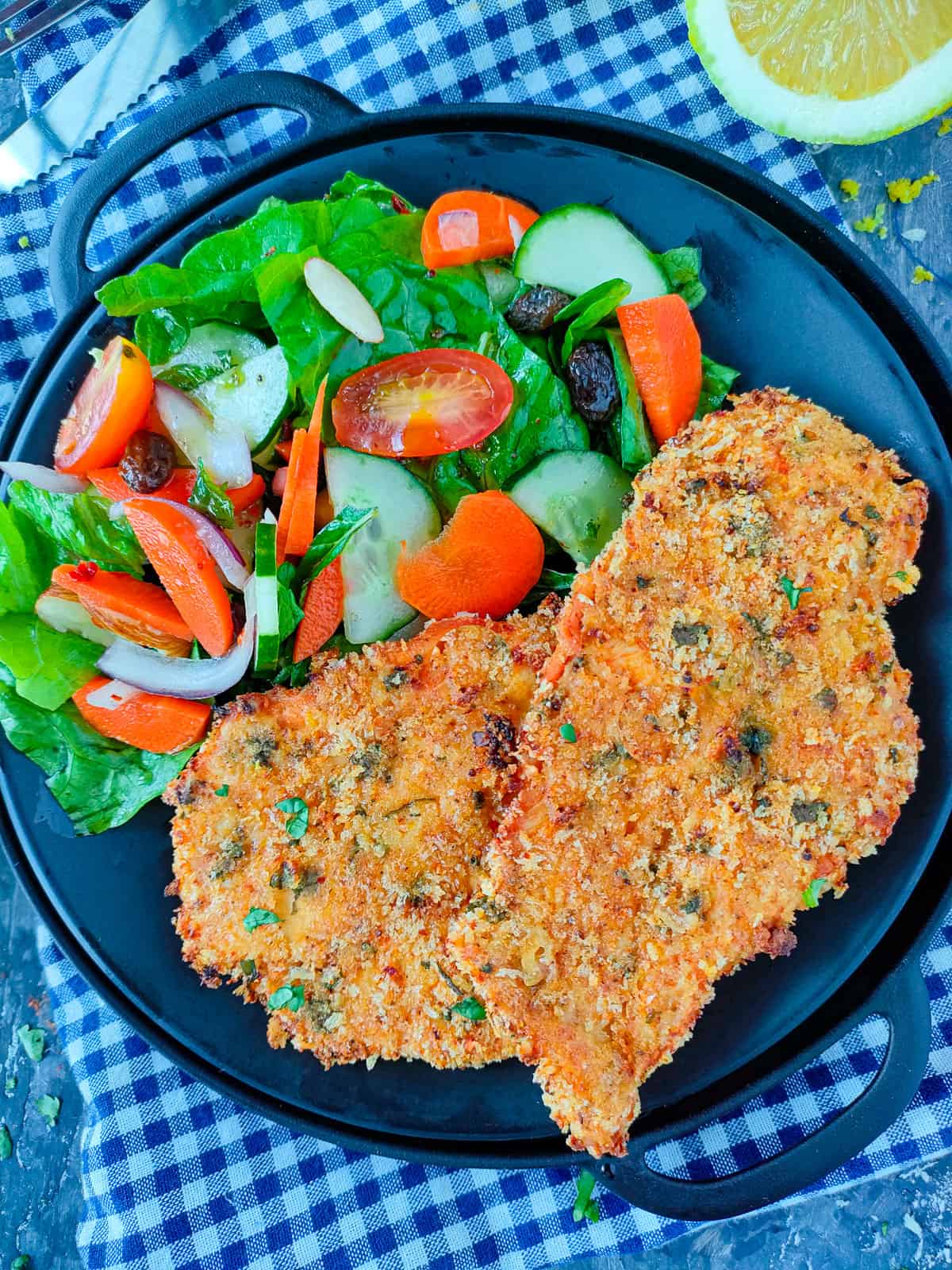 Crispy panko crusted chicken breasts with vegetable salad on a black plate.