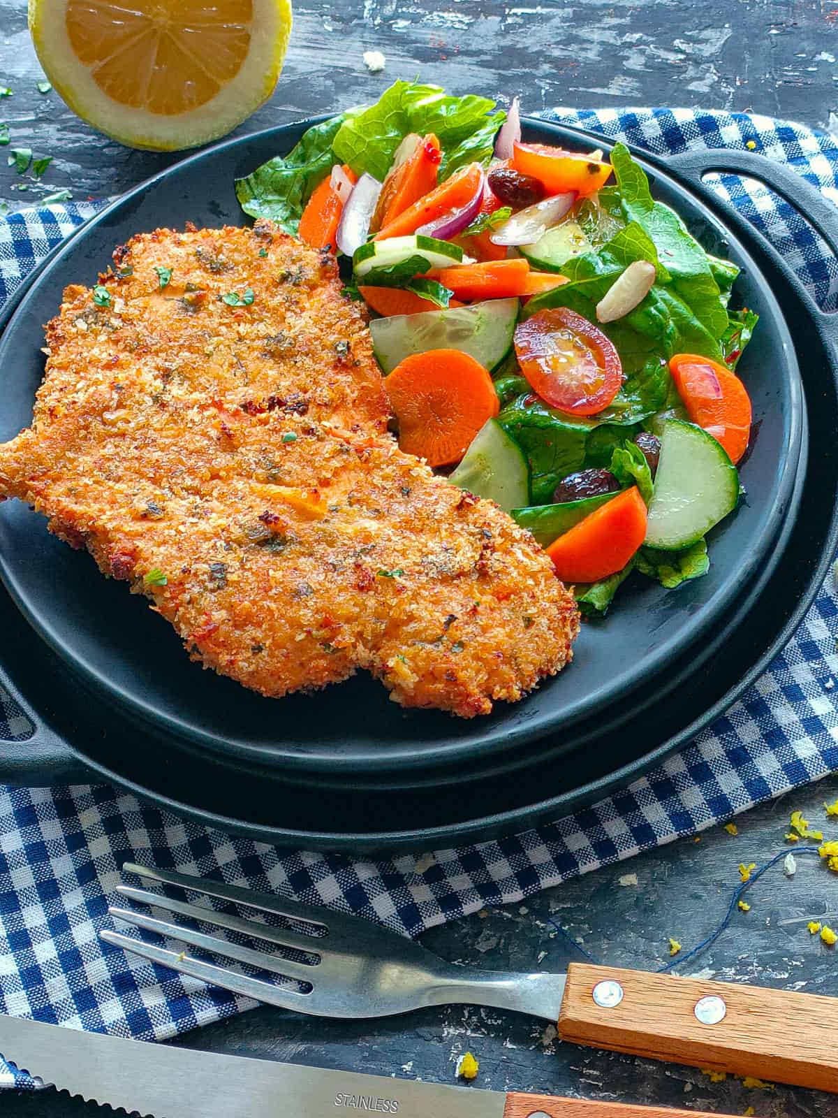 Baked Panko chicken breasts with vegetable salad on a black plate.